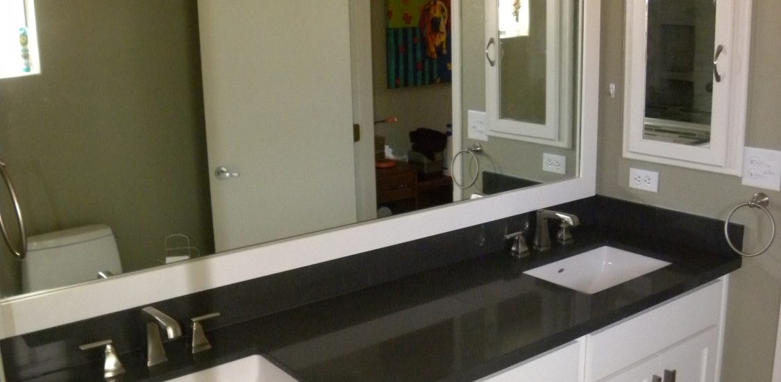After photo of a remodeled bathroom with custom black countertops, white cabinets, and matching mirrors with white trim.