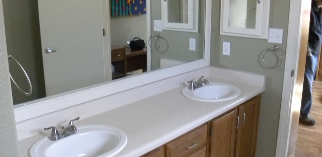 Before photo of a residential bathroom with white countertops and wooden cabinets.