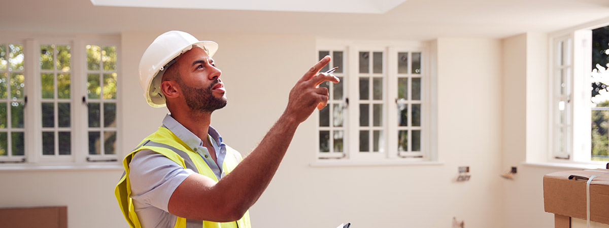 Man Wearing Hard Hat & Yellow Vest Inspecting Home