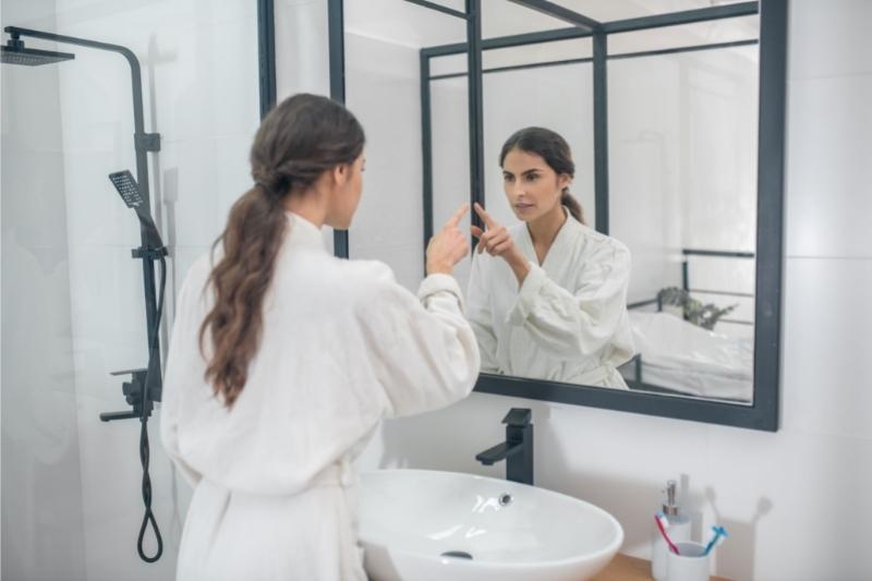woman looking into a mirror deciding if she is capable of remodeling her bathroom