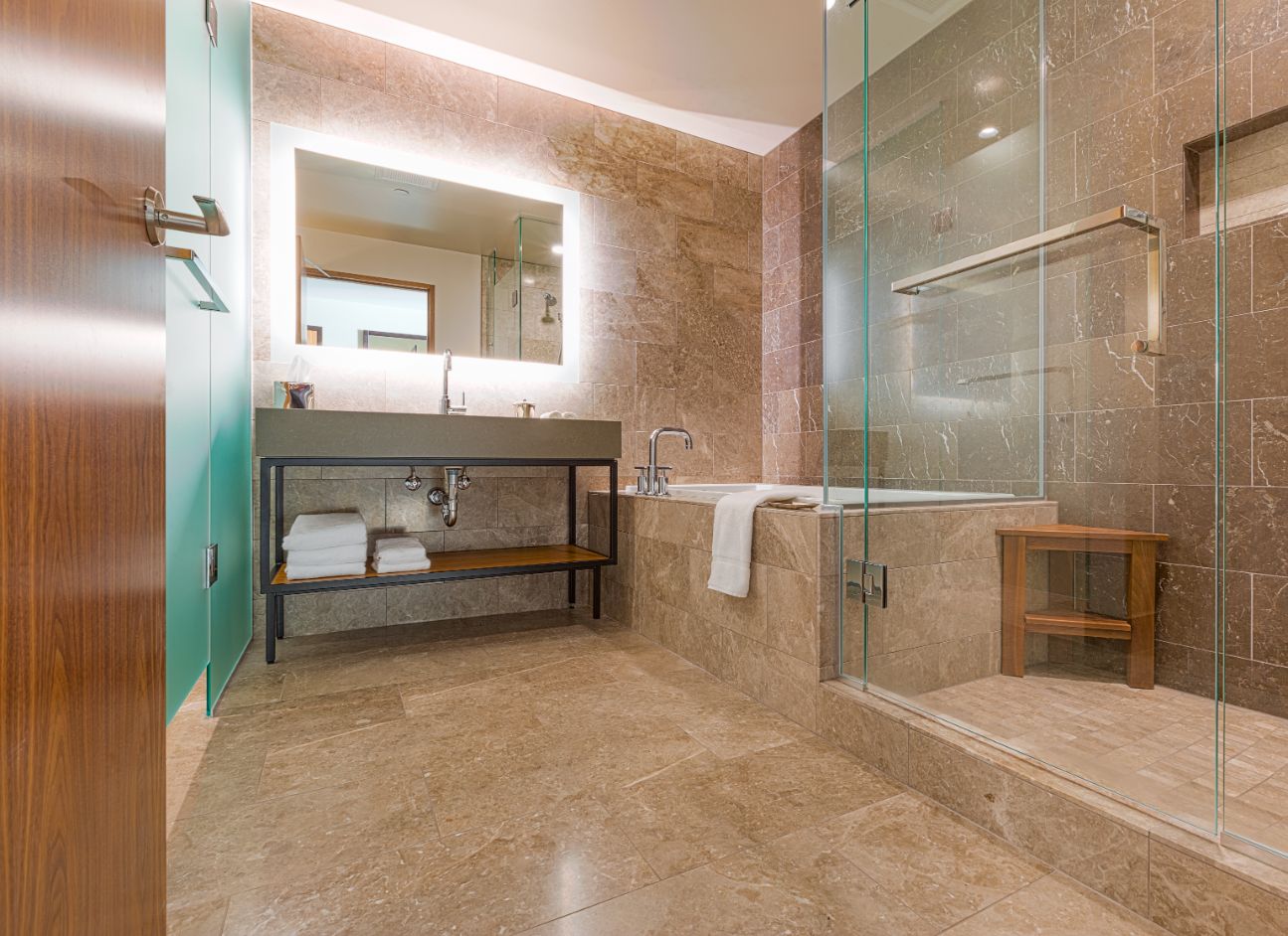 Picture of a modern bathroom featuring a backlit mirror, marble tiles, and warm colors.